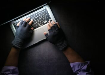 Hände in Handschuhen tippen im Dunkeln auf einem Laptop, Symbolbild zu Phishing
