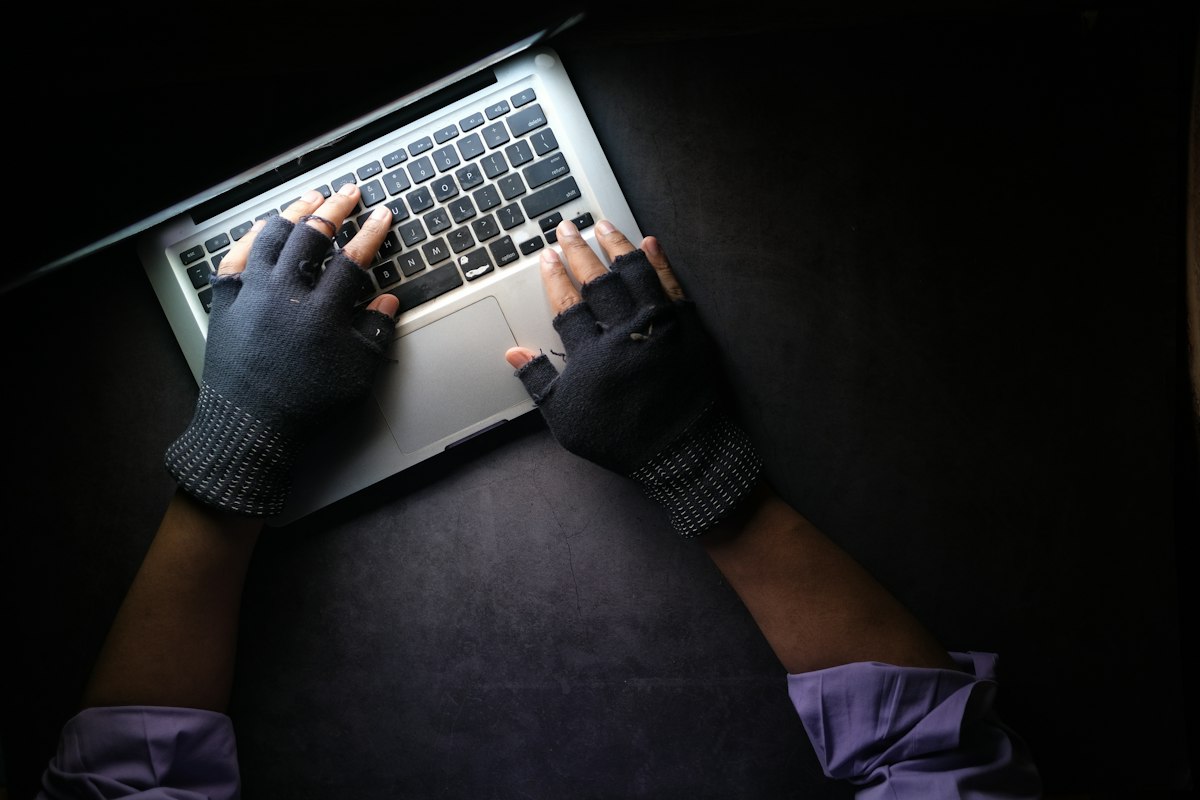 Hände in Handschuhen tippen im Dunkeln auf einem Laptop, Symbolbild zu Phishing